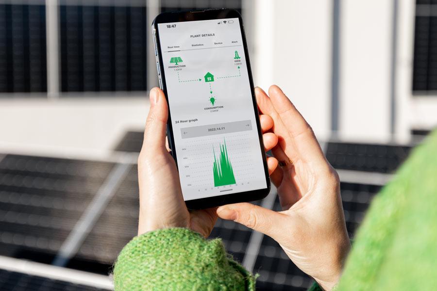 Hands holding a smartphone showing solar production data in front of solar panels